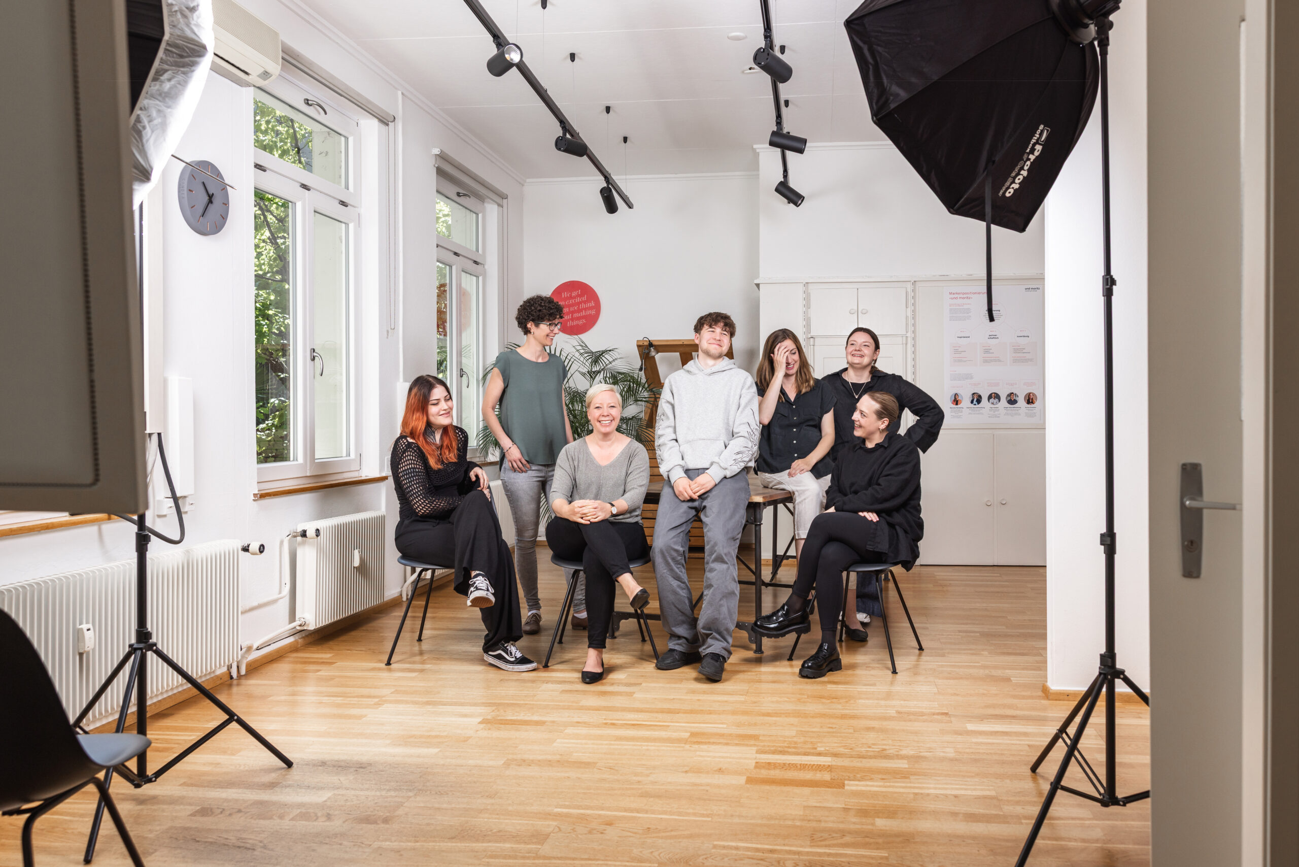 Sieben Personen posieren lächelnd in einem modernen Büro für ein Gruppenfoto mit professioneller Beleuchtung.
